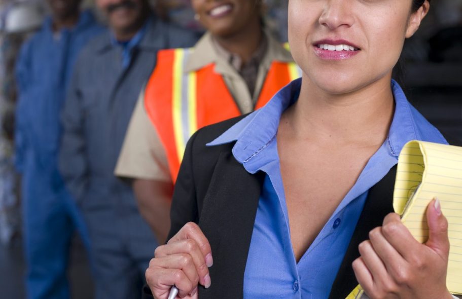 gestion rh Femme en costume avec un carnet, entourée d'hommes en uniformes de travail.